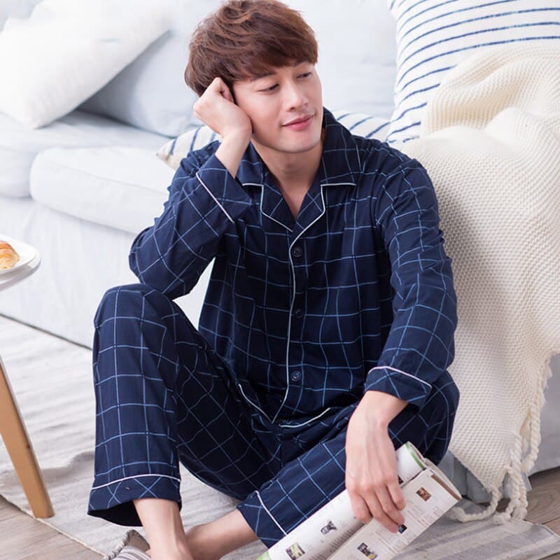 Pyjama carreaux bleu marine décontracté en coton pour hommes très haute qualité porté par un homme assis sur un tapis devant un lit dans une maison