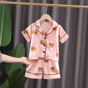 Pyjama d’été rose en coton motif ours pour enfants sur une ceintre dans une maison