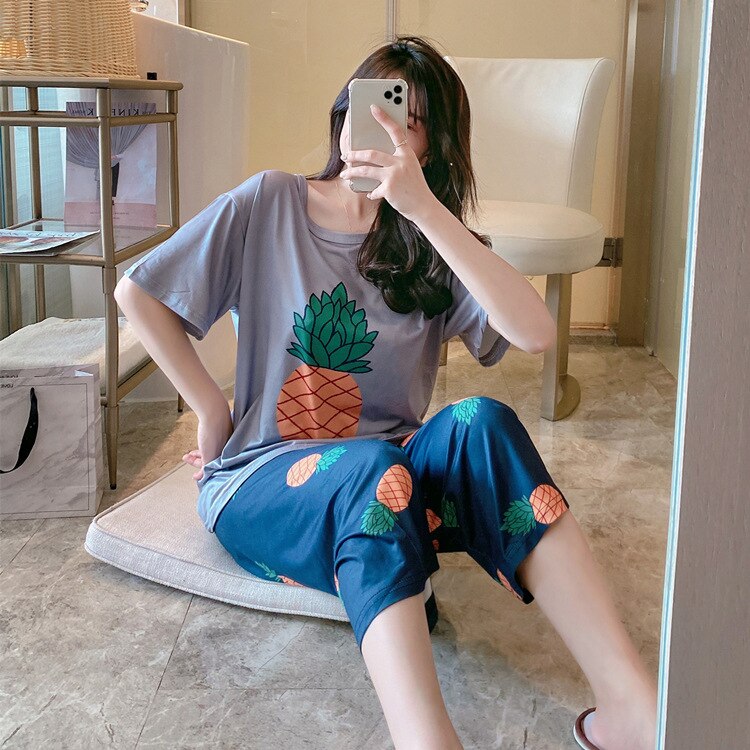 Pyjama deux pièces cou rond motif ananas porté par une femme assise sur un oreiller devant un miroir
