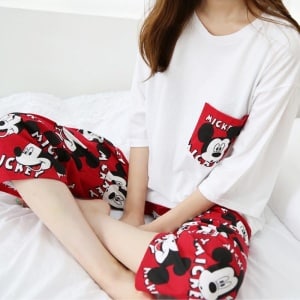 Pyjama deux pièces rouge et blanc motif Mickey porté par une femme assise sur un lit à la mode