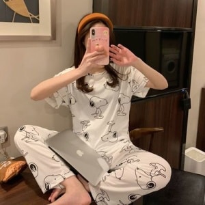 Pyjama deux pièces manches courtes motif Chien porté par une femme assise qui prend une photo dans une maison