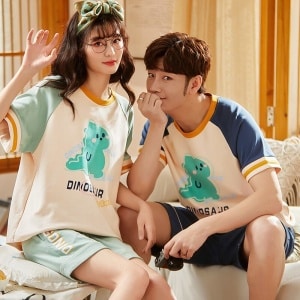Pyjama deux pièces en coton t-shirt et short motif Dinosaure porté par une couple assise sur un lit dans une maison