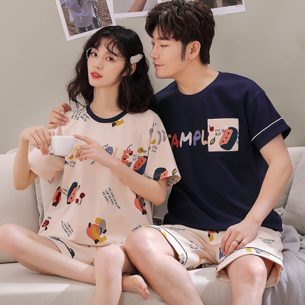 Pyjama deux pièces en coton t-shirt et short motif bande dessinée porté par une couple assise sur un canapé dans une maison