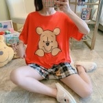 Pyjama deux pièces t-shirt motif Winnie et short carreau à la mode portée par une femme assise sur un carreau dans une maison