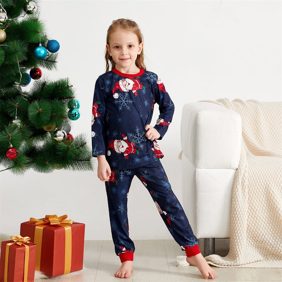 Pyjama imprimé flocon de neige et Père Noël pour la famille porté par une petite fille devant un arbre de noël dans une maison