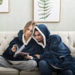 Sweat Plaid – Le Pull Plaid Ultra Confortable pour couple très haute qualité porté par une couple assise sur un canapé dans une maison