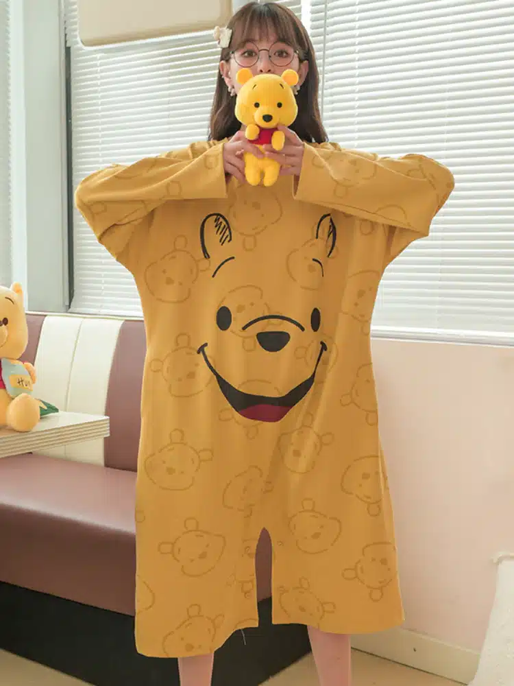 Pyjama ample de Winnie l'ourson pour femme jaune moutarde porté par une femme devant un canapé dans une maison