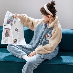 Pyjama bleu clair pour couple en polaire porté par une femme assise sur un canapé dans une maison