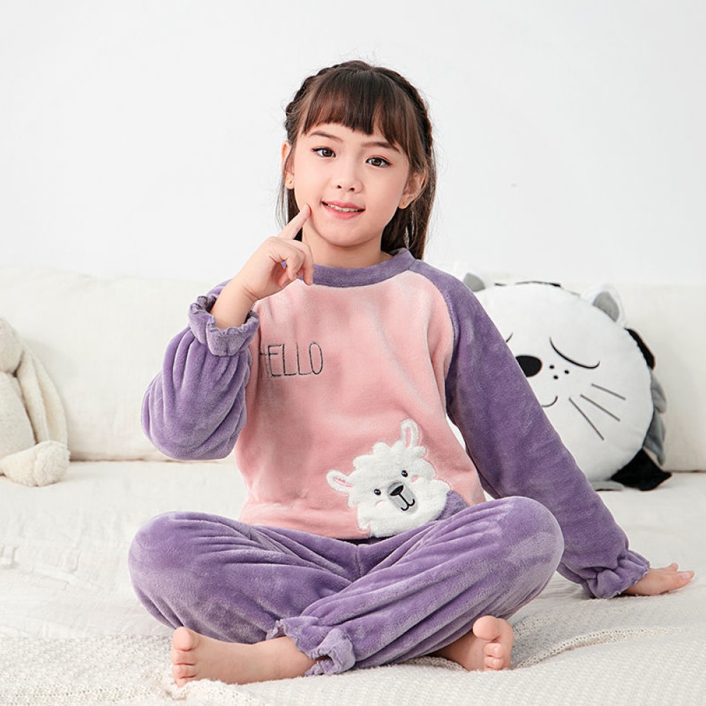 Ensemble pyjama polaire pour enfants violet porté par une petite fille assise sur un lit dans une maison