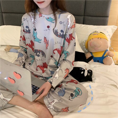 Pyjama automne manches longues à motif chats pour femmes portée par une femme assise sur un lit dans une maison