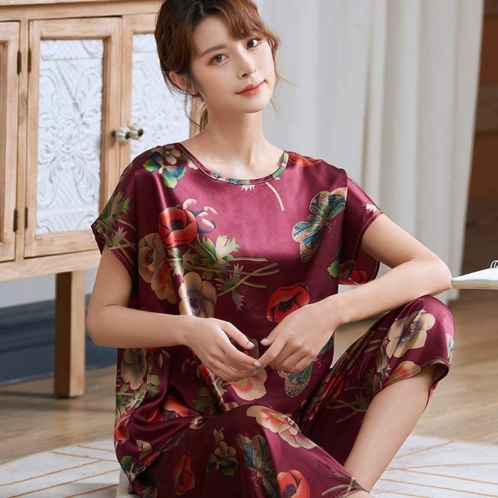 Pyjama d'été rouge en satin de soie avec imprimé fleurs pour femmes portée par une femme assise sur un tapis dans une maison