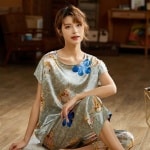 Pyjama d'été gris deux pièces en satin de soie avec imprimé floral à la mode portée par une femme assise sur un tapis dans une maison