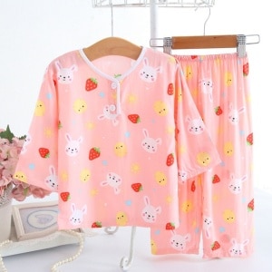 Pyjama deux pièces en coton à motif fraise et lapin pour enfant rose sur une ceintre dans une maison