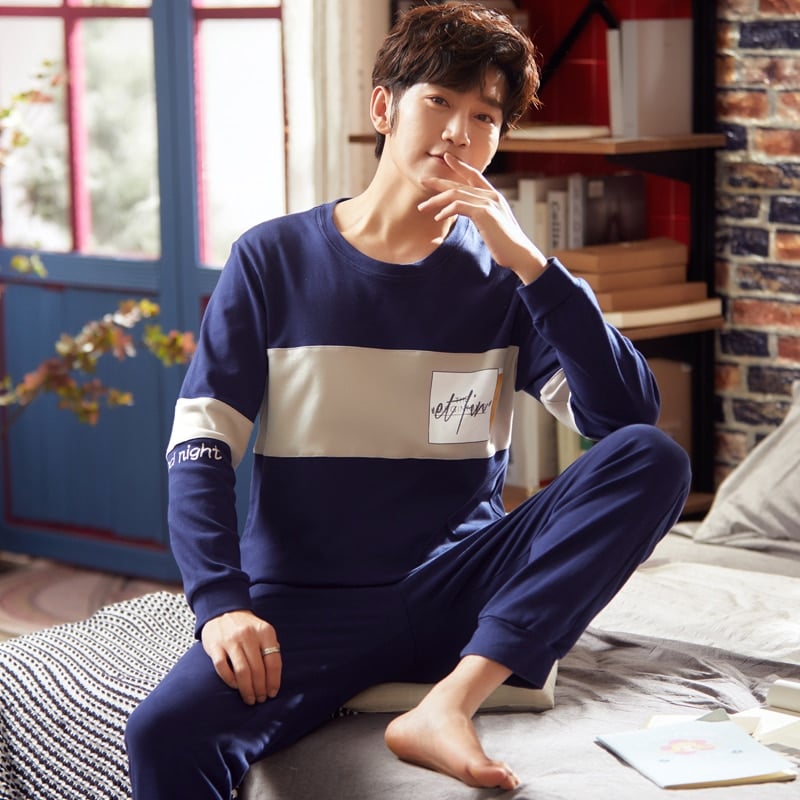 Pyjama en coton bleu marine deux pièces à manches longues portés par un homme assise sur un lit dans une maison