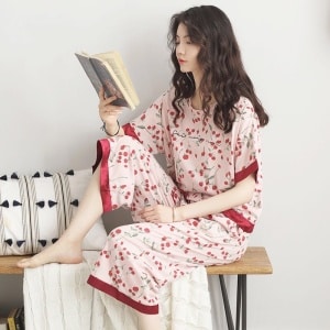 Pyjama femme à manche chauve-souris avec imprimé fleurs rouges portée par une femme sui lis une livre assise sur une chaise dans une maison