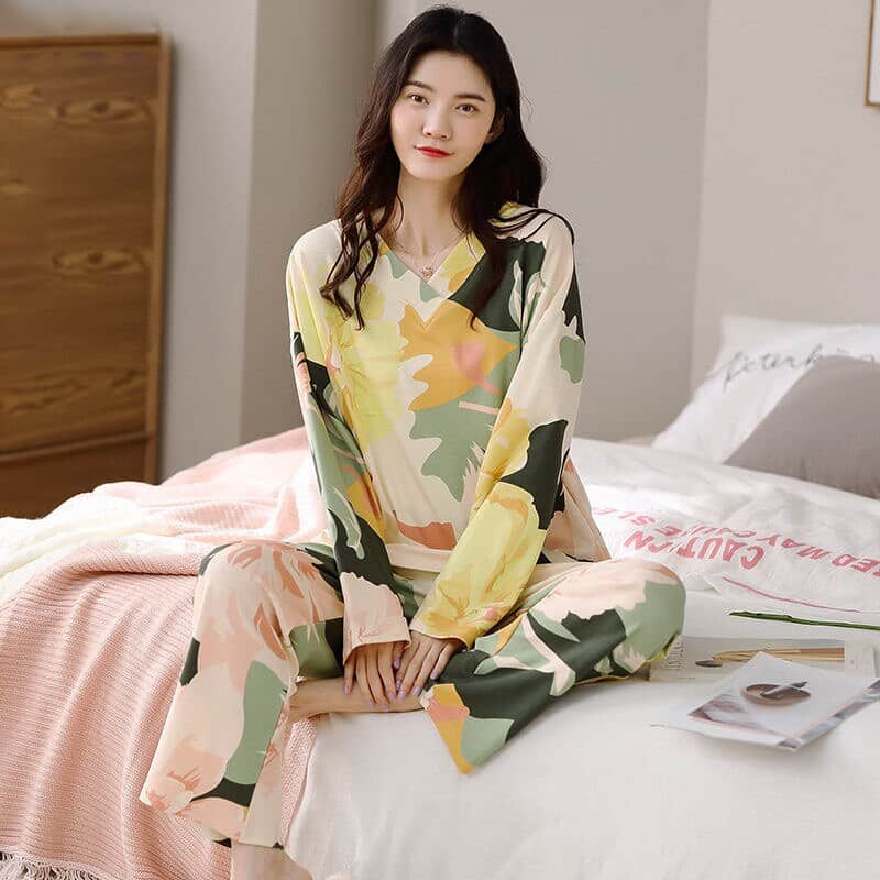 Pyjama femme à manches longues avec col en V et motif floral porté par une femme assise sur un lit dans une maison