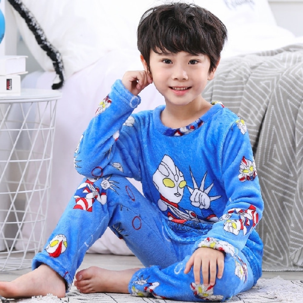 Pyjama bleu en flanelle à motif super-héros pour garçon bleue porté par un petit garçon assise sur un tapis devant un lit dans une maison