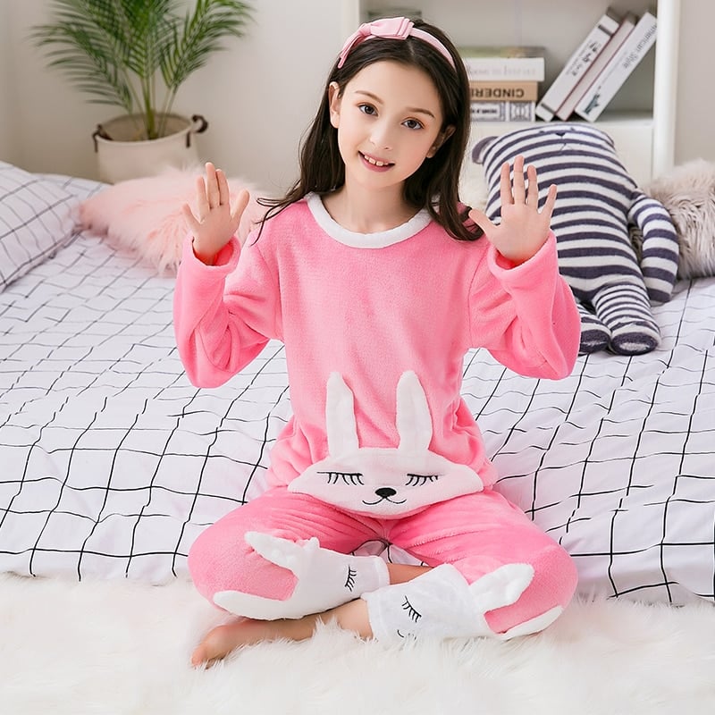 Pyjama rose en flanelle avec imprimé lapin pour fille portée par une fille qui porte une serre tête assise sur un lit dans une maison