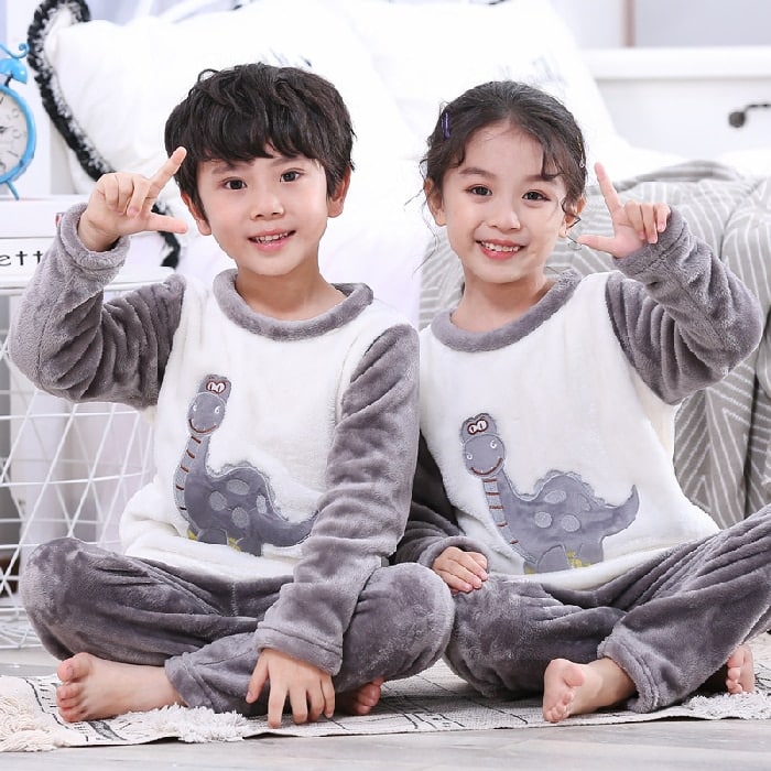 Pyjama gris deux pièces en flanelle à motif dinosaure pour enfant porté par un petit garçon et une petite fille dans une maison