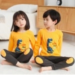 Pyjama pour enfant avec pull jaune à motif dinosaure et pantalon marron avec deux enfants qui porte le pyjama
