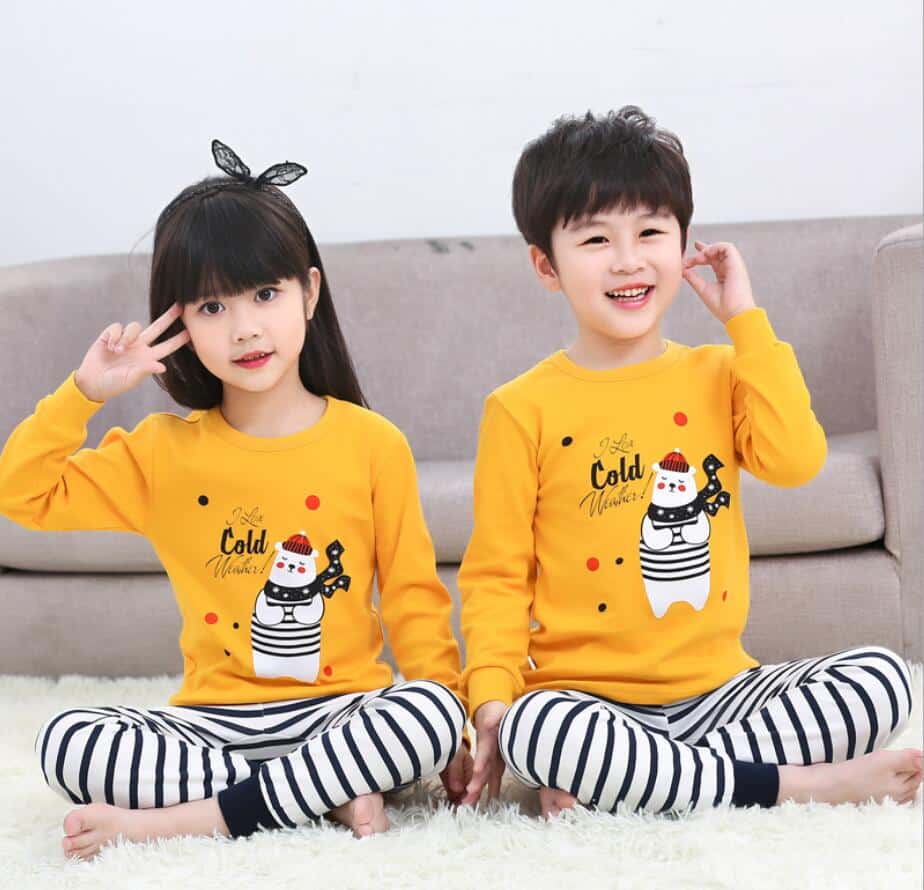 Pyjama printemps avec pull-over jaune et pantalon blanc rayé noir avec deux enfants qui porte le pyjama et un fond un canapé