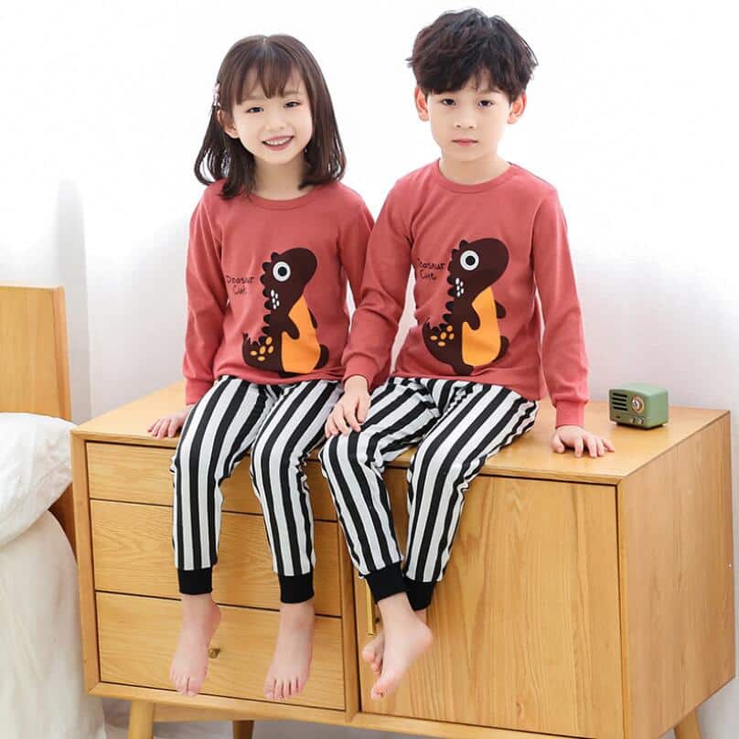 Pyjama printemps avec pull rose et pantalon blanc rayé noir pour enfants avec deux enfants qui porte le pyjama et qui sont sur le meuble