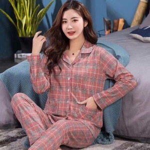 Pyjama carreaux deux pièces à col rabattu pour femmes à la mode portée par une femme assise sur un tapis devant un lit dans une maison