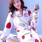 Pyjama en molleton de corail à motif fraise pour femmes très à la mode, porté par une femme assise sur un lit dans une maison