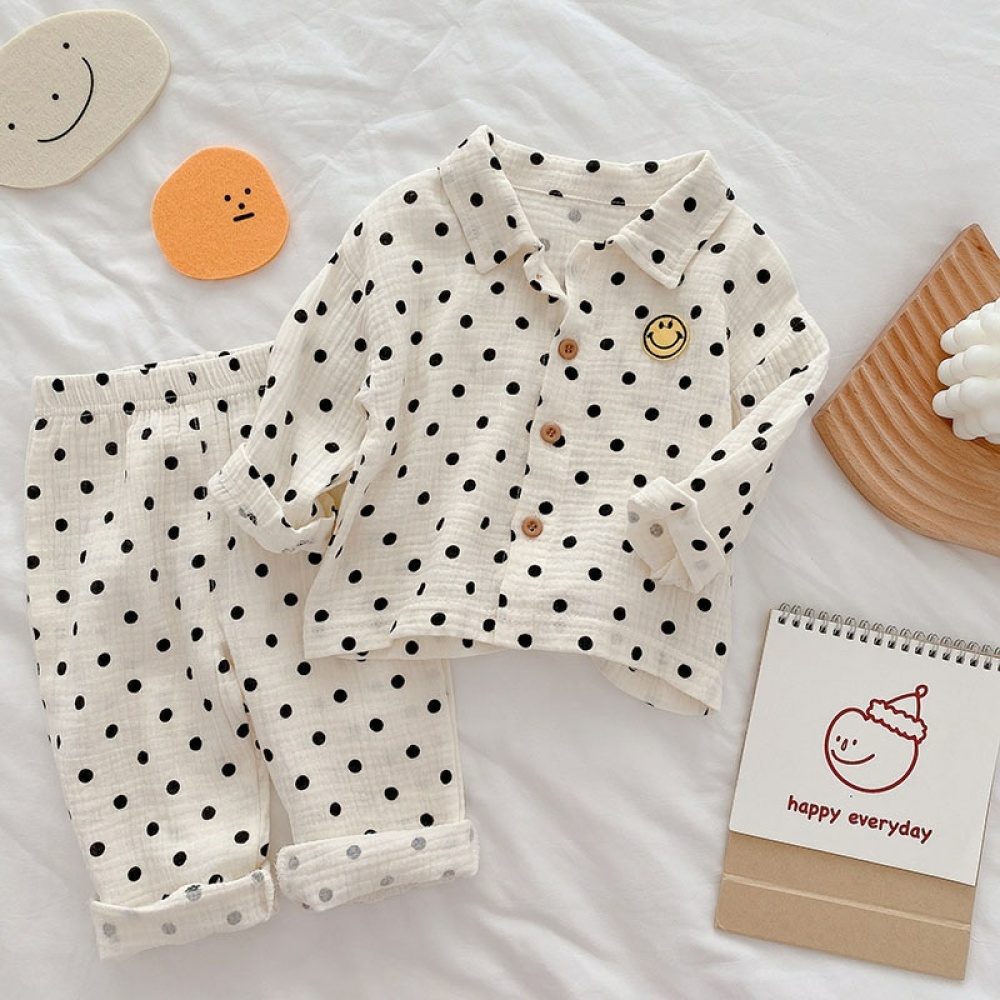 Pyjama pour enfant blanc à pois noir avec un logo smiley jaune posé sur un drap blanc avec des petits jouets autour