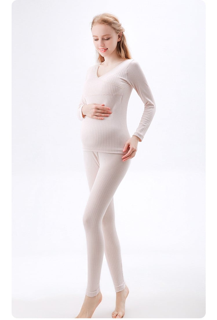 femme enceinte en train de se toucher le ventre d'une main , porte un pyjama beige composé d'un pantalon et d'un pull manche longue