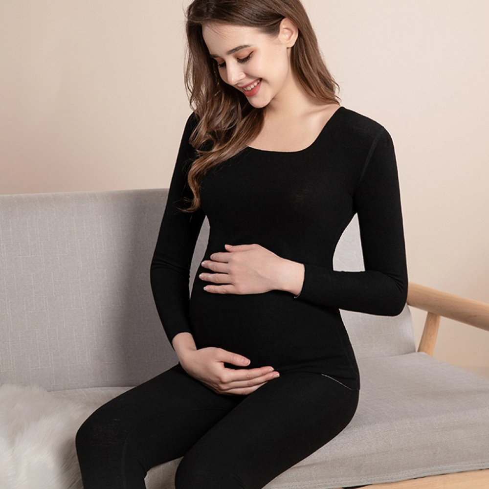 jeune femme enceinte assise porte un pyjama noir de grossesse , elle sourit en touchant son ventre rond