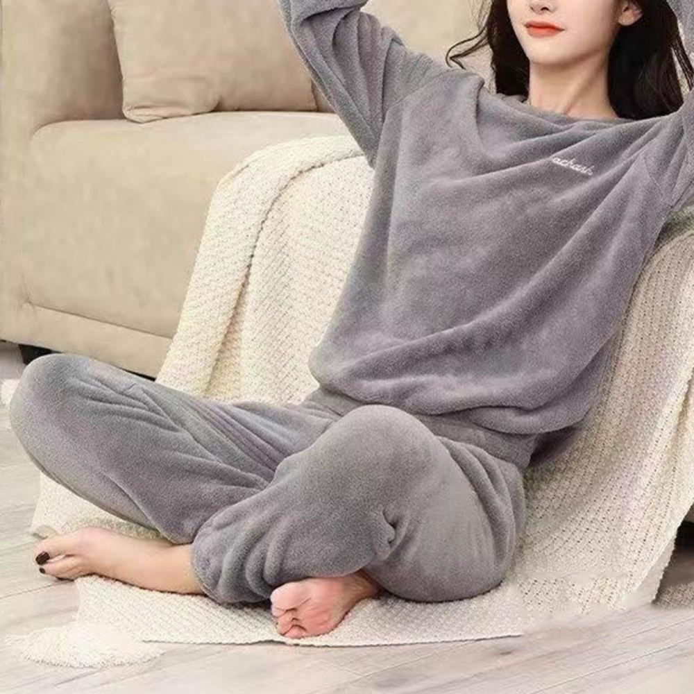 jeune femme porte un pyjama en pilou pilou gris, elle est assise sur un plaid près d'un canapé , par terre, les mains croisées derrière sa tête