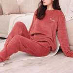 jeune femme porte un pyjama en pilou pilou rouge, elle est assise sur un plaid près d'un canapé , par terre